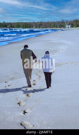 Ein älteres Paar, das Hand in Hand am langen Sandstrand spazieren geht Stockfoto