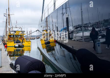 Reflexionen von Arbeitsbooten und Yachthafen, in dem unglaublich polierten Rumpf einer mehrere Millionen Pfund schweren Super-Yacht, die in Falmouth festgemacht ist. Spiegel der Welt Stockfoto