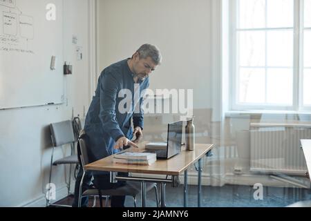 Männlicher Lehrer, der einen Schreibtisch im Klassenzimmer der Universität arrangiert Stockfoto