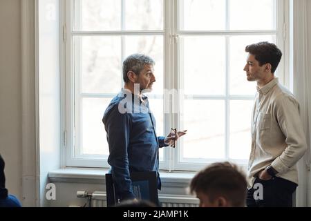 Professor im Gespräch mit einem Studenten in der Nähe von Fenstern in der Universität Stockfoto