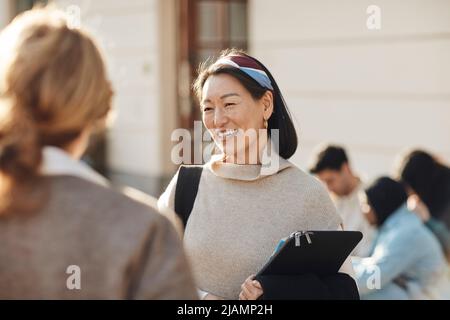 Lächelnde Lehrerin, die die Kollegin auf dem Universitätscampus anschaut Stockfoto
