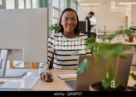 Lächelnde junge afrikanische Geschäftsfrau, die an ihrem Schreibtisch in einem Büro arbeitet Stockfoto