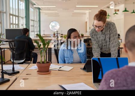 Zwei verschiedene Geschäftsfrauen arbeiten zusammen auf einem Tablet in einem Büro Stockfoto