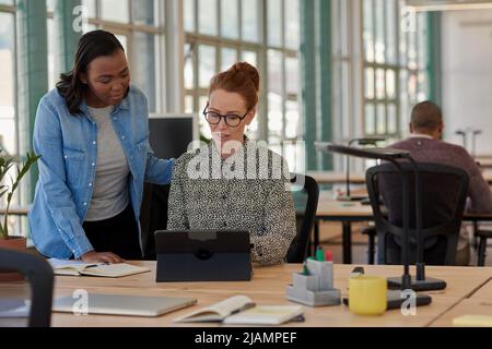 Zwei verschiedene Geschäftsfrauen, die gemeinsam in einem Büro an einem Tablet arbeiten Stockfoto