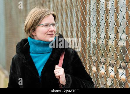 Porträt einer 30-jährigen weißen Frau, die gegen einen Industriezaun posiert und einen schwarzen pelzigen Mantel trägt, Anderlecht, Belgien Stockfoto