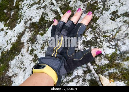 Frau Hand mit lila Nagellack und Via Ferrata Halbfinger Handschuhe, oder abgeschnitten Handschuhe, trägt ein gelbes Smart Armband, über einem Metallkabel A platziert Stockfoto