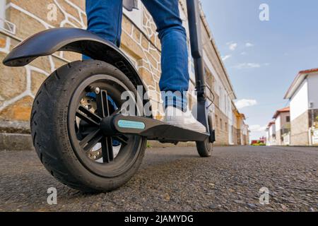 Beine und Füße eines jungen Mannes auf einem Elektroroller auf der Straße von hinten gesehen Stockfoto