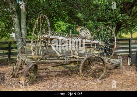 Alte rostige, von Pferden gezogene Heuraken-Farm-Ausrüstung auf einem kaputten Vintage-Wagen, der an einem sonnigen Tag auf einem Bauernhof im Freien aufgegeben wurde Stockfoto