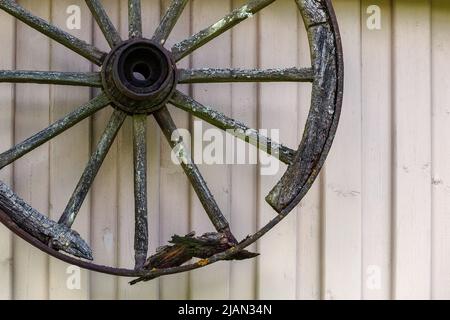 Vintage gebrochenes, verfaultes Holzkutschenrad an der Holzwand des Hauses Stockfoto