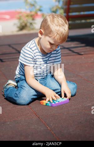 Das Kind kniet auf den Boden des Spielplatzes und spielt zur Entspannung mit einem bunten Spielzeug. Stockfoto