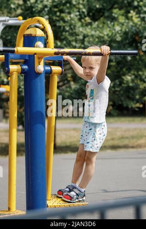 Der kleine Junge trainiert auf einem Outdoor-Fitnessgerät. Stockfoto