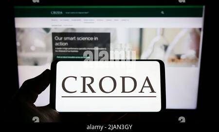Person, die Mobiltelefon mit dem Logo des chamicalen Unternehmens Croda International plc auf dem Bildschirm vor der Business-Webseite hält. Konzentrieren Sie sich auf die Telefonanzeige. Stockfoto
