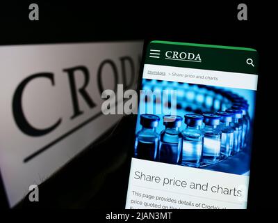 Person, die Mobiltelefon mit der Webseite des chamicalen Unternehmens Croda International plc auf dem Bildschirm vor dem Logo hält. Konzentrieren Sie sich auf die Mitte des Telefondisplays. Stockfoto