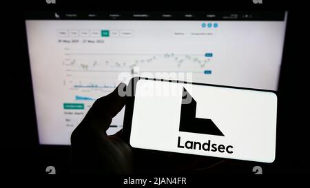Person, die ein Mobiltelefon mit dem Logo der Firma Land Securities Group plc (Landsec) auf dem Bildschirm vor der Webseite hält. Konzentrieren Sie sich auf die Telefonanzeige. Stockfoto