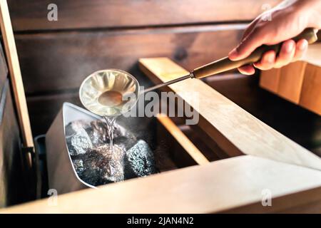 Sauna im finnischen Spa. Heißer Dampf, Wasser auf Steinen. Mann im Wellness- und Gesundheitszimmer in Finnland. Badetherapie bei warmen Temperaturen. Traditionelle Sommerhütte. Stockfoto