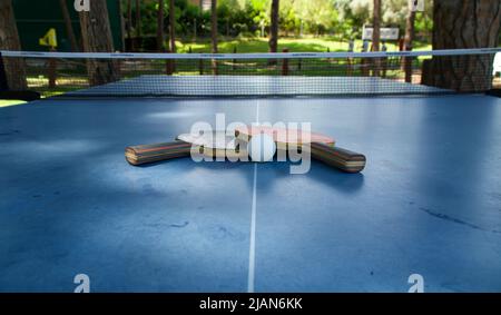 Schläger und Ball auf der blauen Tennistabelle im Freien. Konzept für sportliche Aktivitäten Stockfoto