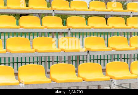Leere Stadionstände, Stühle, gelbe Zuschauersitze in der Kunststoffarena, Detail, kleines Fußballfeld, tagsüber, Nahaufnahme, niemand. Sportveranstaltung Stockfoto
