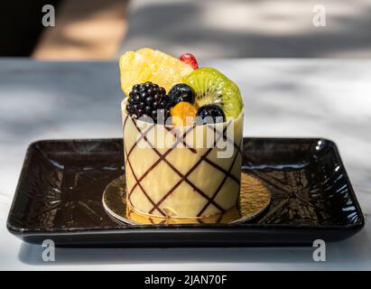 Dessert aus weißer Schokolade mit Früchten auf einem schwarzen Teller Stockfoto