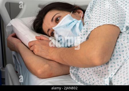 Im Krankenhaus eingewiesenen jungen Frau, die eine Gesichtsmaske trägt, während sie in einem Krankenhausbett liegt Stockfoto