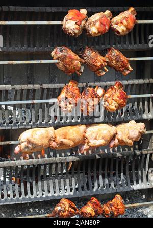 Große industrielle Rotisserie mit Spieß-gebratenen Hühnern und Schweinshaxe und gekochtem Schinkenfleisch beim Kochen im Restaurant des Dorffest Stockfoto