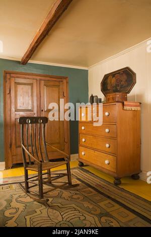 Antiker Schaukelstuhl und Kommode im Hauptschlafzimmer im Obergeschoss im alten, ca. 1810 im kanadischen Cottage-Stil gehaltenen Haus. Stockfoto
