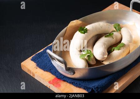 Lebensmittelkonzept hausgemachte Bio-Weißwurst Weisswurst in Aluminium-Schale auf schwarzem Schieferstein mit Kopierfläche Stockfoto