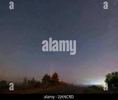 Komet Neowise C2020 F3, wie er im Sommerhimmel über einer Wiese in der Nähe der Landstraße, Region Lviv, Ukraine fliegt. Stockfoto