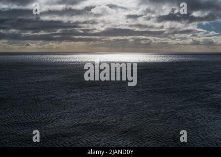 Abendsonne blendet über dem Wasser der Atlantikküste mit leuchtendem Sonnenblend auf der Meeresoberfläche und dem Sonnenuntergangshimmel. Stockfoto