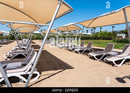 Eine Reihe von Sonnenliegen an einem einsamen Sandstrand im türkischen Resort. Sonnenliegen warten in einem Hotel auf Touristen Stockfoto