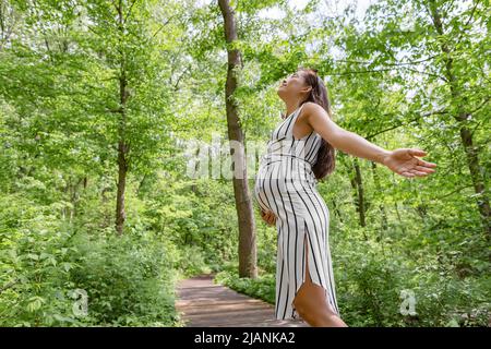 Schwangere glücklich in nachhaltiger Waldnatur im Freien mit offenen Armen in Freiheit. Gesundheits- und umweltfreundliches Umweltschutzkonzept. Schwangerschaft Stockfoto