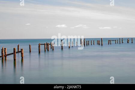 Ein breites, minimalistisches Bild von Swanage alten Pier-Pfosten in einer langen Belichtung noch Meer und blassen Himmel Stockfoto