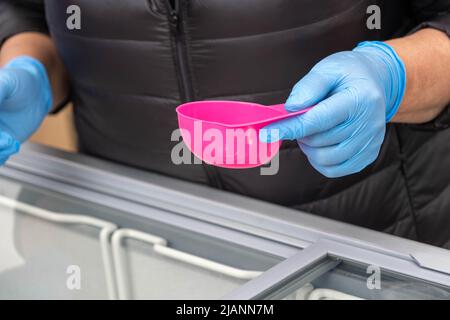 Eisverkäufer mit blauen Gummihandschuhen serviert Eis in einer kleinen rosafarbenen Schale. Stockfoto