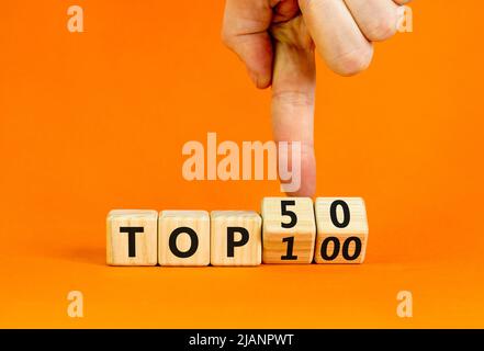 Von Top 100 bis 50 Symbol. Geschäftsmann dreht Holzwürfel und ändert die Begriffe Top 100 zu Top 50. Schöner orangefarbener Tisch und Hintergrund. Unternehmen Stockfoto