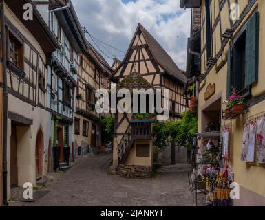 Eguisheim, Frankreich - 29. Mai 2022: Enge gepflasterte Straße mit bunten historischen Fachwerkhäusern Stockfoto