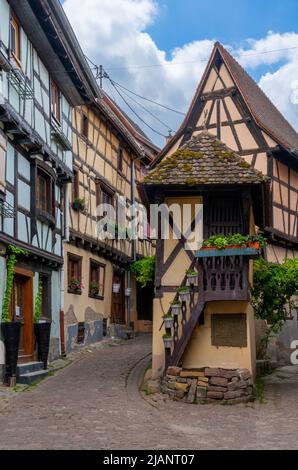 Eguisheim, Frankreich - 29. Mai 2022: Enge gepflasterte Straße mit bunten historischen Fachwerkhäusern Stockfoto