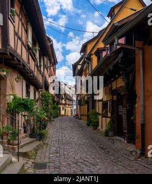 Eguisheim, Frankreich - 29. Mai 2022: Enge gepflasterte Straße mit bunten historischen Fachwerkhäusern Stockfoto