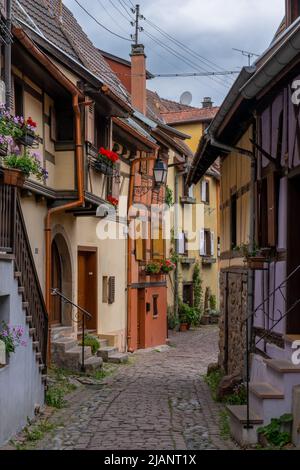 Eguisheim, Frankreich - 29. Mai 2022: Enge gepflasterte Straße mit bunten historischen Fachwerkhäusern Stockfoto