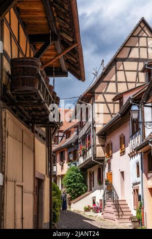 Eguisheim, Frankreich - 29. Mai 2022: Enge gepflasterte Straße mit bunten historischen Fachwerkhäusern Stockfoto