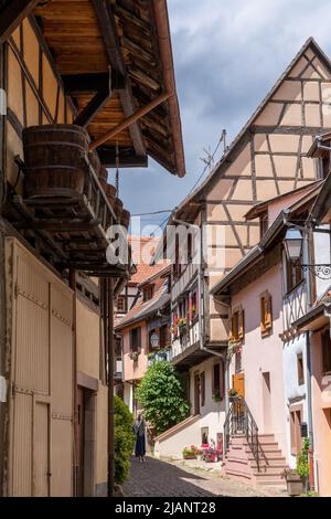 Eguisheim, Frankreich - 29. Mai 2022: Enge gepflasterte Straße mit bunten historischen Fachwerkhäusern Stockfoto