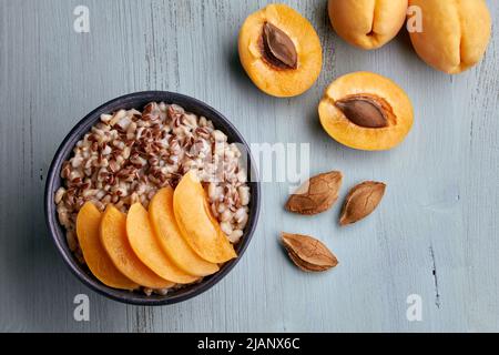 Vollkorn-Haferflocken mit Aprikosenstücken und Aprikosenhälften auf einem bemalten blauen Holztisch. Veganes Frühstück. Draufsicht. Flach liegend Stockfoto