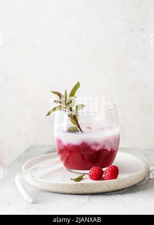 Hausgemachter Buttermilch-Smoothie mit Himbeermarmelade mit Pfefferminzzweig in einem Glas. Gesunde süße Lebensmittel Konzept Copy space. Stockfoto
