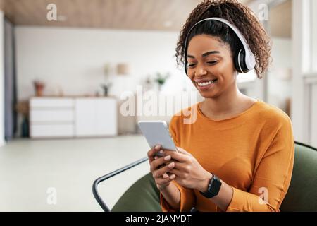 Lächelnde schwarze Dame mit Kopfbedeckung und Handy Stockfoto