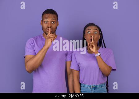 Schwarzes Paar, das Finger auf die Lippen stampft und ein Zeichen für die Stille macht Stockfoto