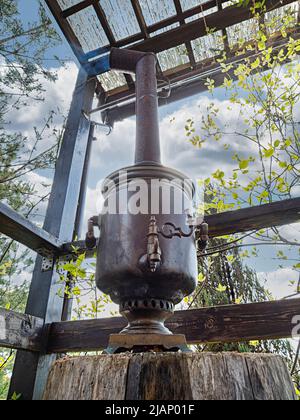 Russischer Samowar im Vintage-Stil auf der Terrasse eines Landhauses. Das in den Samowar gegossene Wasser wird durch das Feuer im inneren Rohr erhitzt Stockfoto