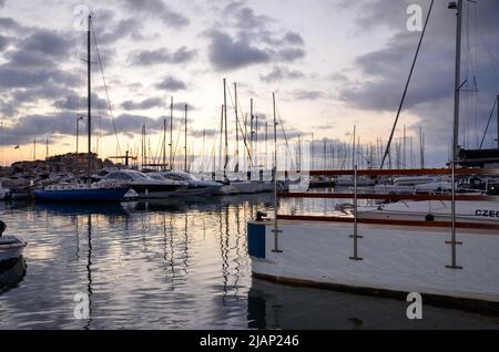 Yachten und Segelschiffe im Hafen von Denia unter leicht bewölktem, farbenfrohem Sommernachtshimmel mit dem Burgberg und dem Schloss von Denia im Hintergrund Stockfoto