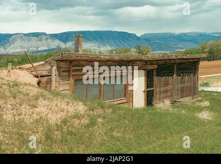 Alte Hühnerstall aus Holz mit Fenstern ist aus dem Untergrund gebaut. Erde bedeckt das Dach. Im Inneren werden Hühner hinter einem Holzstäbchen-Zaun gehalten. Stockfoto