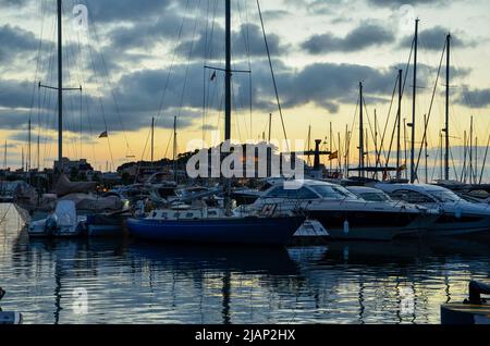 Yachten und Segelschiffe im Hafen von Denia unter leicht bewölktem, farbenfrohem Sommernachtshimmel mit dem Burgberg und dem Schloss von Denia im Hintergrund Stockfoto