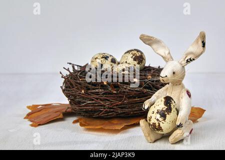 Plüschhase und Wachtel haben Eier in einem Nest auf einem weißen Holzhintergrund getupft. Osterkonzept Stockfoto