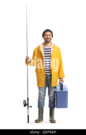 Junger Mann in einem Regenmantel und Stiefeln mit einer Angelrute und einem Kühlschrank isoliert auf weißem Hintergrund Stockfoto