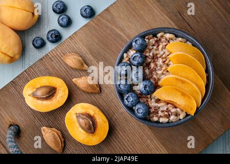 Vollkorn-Haferflocken mit Leinsamen, Heidelbeeren und Aprikosen-Keilen in einer Schüssel auf einem Holztablett. Energy Breakfast Stockfoto